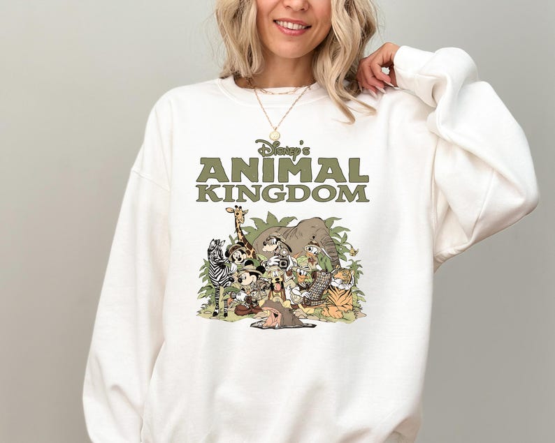 May include: White crew neck sweatshirt with the text "Disney's Animal Kingdom" in green. The graphic features cartoon animals including a zebra, giraffe, elephant, and tiger. The sweatshirt is a casual style.