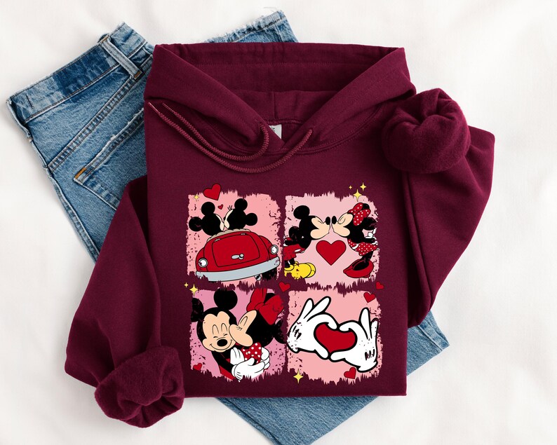 May include: Burgundy hoodie with a graphic of Mickey and Minnie Mouse in romantic scenes. The design includes a red car, hearts, and the couple kissing. The hoodie is displayed on a pair of blue jeans.