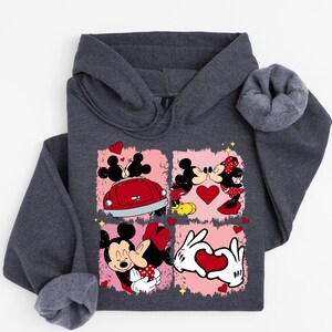 May include: Dark grey hooded sweatshirt with a graphic of Mickey and Minnie Mouse in romantic poses. The design includes hearts, a red car, and the characters kissing. The sweatshirt is made of a soft material.