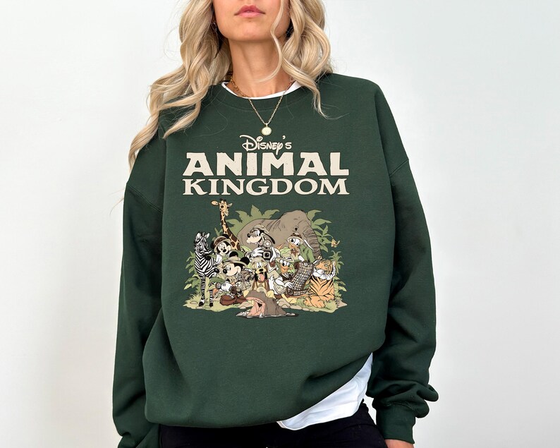 May include: Dark green sweatshirt with the text "Disney's Animal Kingdom" in cream. The graphic below features cartoon animals such as a zebra, giraffe, and tiger. The sweatshirt has a white collar.