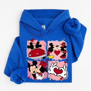 May include: A royal blue hooded sweatshirt with a graphic of Mickey and Minnie Mouse in romantic poses. The design includes a red car, hearts, and the characters kissing. The sweatshirt is made of a soft material.