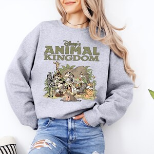 May include: A grey sweatshirt with the text "Disney's Animal Kingdom" in green, and a colourful graphic of cartoon animals. The design includes a giraffe, zebra, elephant, tiger, and other characters.