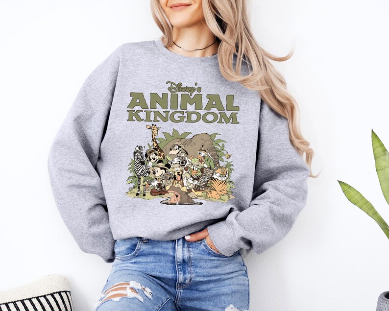 May include: A grey sweatshirt with the text "Disney's Animal Kingdom" in green, and a colourful graphic of cartoon animals. The design includes a giraffe, zebra, elephant, tiger, and other characters.