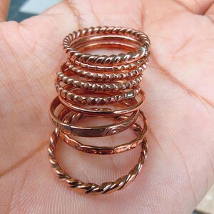 Puede incluir: Una pila de anillos de color cobre con varios dise&ntilde;os. Los anillos incluyen patrones trenzados, con cuentas y grabados. Los anillos est&aacute;n apilados, mostrando las diferentes texturas y estilos.