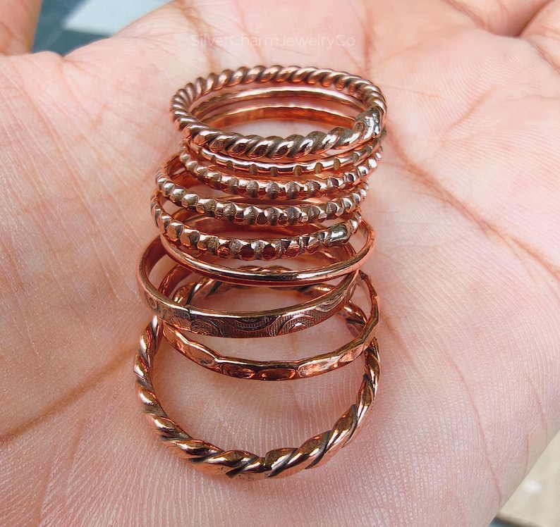 Puede incluir: Una pila de anillos de color cobre con varios dise&ntilde;os. Los anillos incluyen patrones trenzados, con cuentas y grabados. Los anillos est&aacute;n apilados, mostrando las diferentes texturas y estilos.