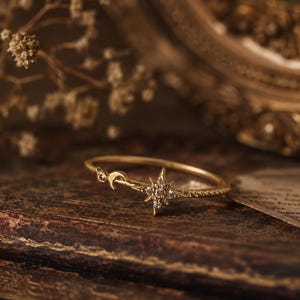 Peut inclure: Une bague dorée composée d'un anneau fin orné d'un petit croissant de lune et d'un motif central en forme d'étoile incrusté de minuscules pierres transparentes. L'anneau en métal poli s'affine vers les éléments de design célestes.