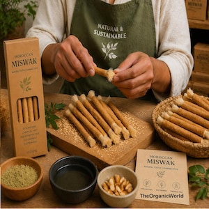 Op de afbeelding: Een presentatie van Marokkaanse Miswak natuurlijke tandenreinigingsstokjes. De afbeelding toont een persoon die de stokjes klaarmaakt, met een doos van 10 stokjes, een houten snijplank en een mand gevuld met meer stokjes. De tekst op de doos luidt "100% Natuurlijk, Chemievrij, Zonder conserveringsmiddelen, Milieuvriendelijk, Duurzaam."
