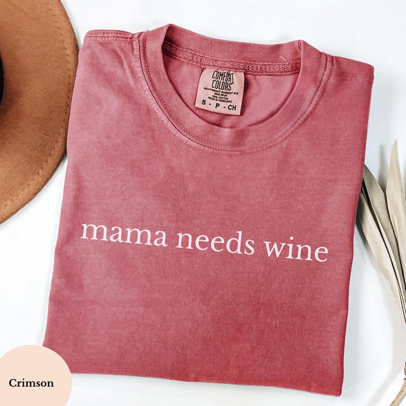 May include: Crimson Comfort Colors t-shirt with the white text "mama needs wine". The t-shirt has a crew neck and short sleeves. The label reads "S - P - CH".