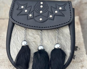 Può includere: Un sporran in pelle nera con patta decorativa con borchie argentate e design in rilievo. Lo sporran ha un corpo in pelliccia grigia e bianca e tre nappe di pelliccia nera appese a catene d'argento.
