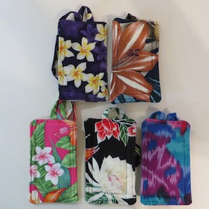 Peut inclure: Cinq &eacute;tuis de t&eacute;l&eacute;phone en tissu avec poign&eacute;es, chacun avec un motif floral unique. Les motifs comprennent des plumeria blancs et jaunes sur fond violet, un lis orange sur fond marine, des fleurs roses et blanches sur fond rose, des fleurs rouges sur fond noir et un ikat bleu et violet.