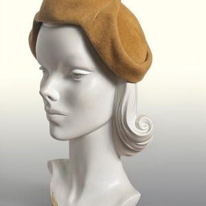 Puede incluir: Una boina de fieltro color canela con un diseño de ala plegada y estructurada. El sombrero presenta una textura suave y mate con una corona redondeada que se asienta firmemente. El material parece suave y uniforme, ofreciendo una silueta limpia.