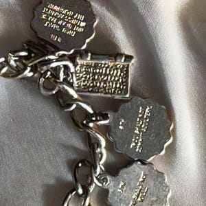 May include: A silver charm bracelet with a basket charm and three scalloped-edge charms. The charms have engraved text. The bracelet is on a white surface.