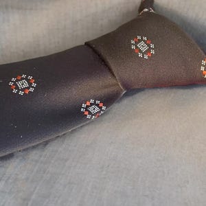 May include: A dark brown tie featuring a repeating pattern of small, stylized floral designs in red, white, and black. The tie is made of a smooth fabric and is knotted at the top.