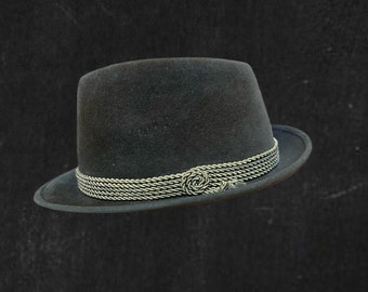 May include: A dark gray fedora hat with a decorative silver-colored band around the crown. The band features a woven design and a small, decorative knot. The hat has a classic, structured shape.