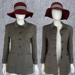 May include: Two mannequins display a matching ensemble: a gray tweed jacket with black buttons and a matching skirt. Each mannequin wears a burgundy hat with a gray band. The jackets have pockets and a classic collar. The background is a light gray.