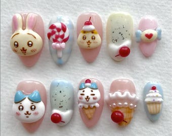 May include: A set of ten artificial nails with various 3D designs. The designs include a bunny, a lollipop, a pudding, a heart, a cat, an ice cream cone, and a cupcake. Each nail has a pink or light blue base color.