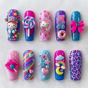 May include: A set of ten press-on nails featuring colorful 3D designs including a Hello Kitty figure, a lollipop, a gummy bear, a donut, a pink bow, lips with a lollipop, a rainbow, a crescent moon, stars, hearts, and leopard print patterns.