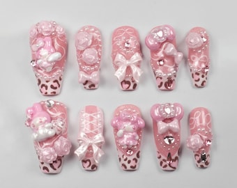 May include: A set of ten pink artificial nails with various designs. Some nails feature bows, pearls, and floral accents. Others have 3D figures and leopard print tips. The nails are arranged on a white surface.