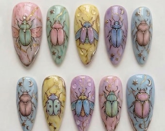 Puede incluir: Un juego de diez uñas postizas en forma de almendra con ilustraciones de escarabajos pintadas a mano sobre fondos con efecto mármol en tonos pastel rosa, amarillo, azul y morado, decoradas con vetas doradas, estrellas y lunas crecientes.