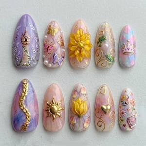 May include: A set of ten almond-shaped artificial nails with intricate designs. The nails feature a variety of themes, including a tower, butterflies, a large yellow flower, chameleons, a crown, a golden braid, a sun, lanterns, a heart, and an artist's palette.