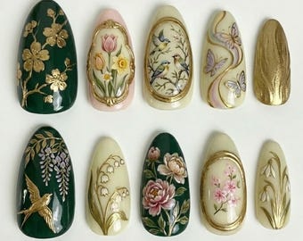 May include: A collection of ten almond-shaped artificial nails with intricate floral and nature-inspired designs. The nails feature gold accents and a variety of colors, including green, pink, and cream. Designs include flowers, birds, and butterflies.