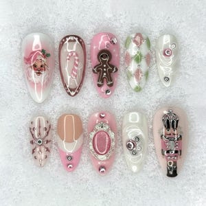 May include: A set of ten artificial nails with various Christmas-themed designs. The nails feature images of Santa Claus, candy canes, gingerbread men, and nutcrackers. Colors include pink, white, brown, and green, with decorative embellishments.