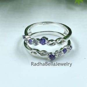 May include: Two silver rings stacked together, each adorned with small, round, purple gemstones. The rings have a delicate, intertwined design. The brand name "RadhaBellaJewelry" is visible at the bottom.