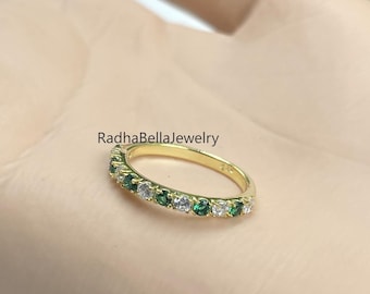 Puede incluir: Un anillo de banda de oro con piedras de esmeralda y diamante alternas. El anillo está colocado en una mano, con el texto "RadhaBellaJewelry" visible.