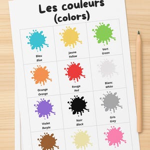Puede incluir: Una tabla de colores titulada "Les couleurs (colors)" con muestras de color en una cuadrícula. Cada muestra es una salpicadura de color con el nombre del color en inglés y francés. Un lápiz de madera descansa en el lado derecho de la tabla.