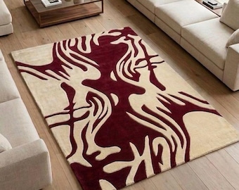 May include: A rectangular area rug featuring a high-contrast, abstract pattern in deep burgundy and cream. The design consists of fluid, organic shapes that flow across the surface, creating a bold visual statement on the light wood floor.