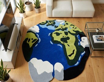 Puede incluir: Una alfombra redonda con un diseño de mapa del mundo. La alfombra presenta un océano azul, continentes verdes y amarillos, y regiones polares blancas y grises. La alfombra está colocada sobre un suelo de madera en un salón.