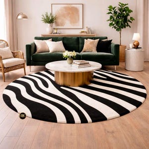 May include: A round rug with a bold zebra stripe pattern in black and white. The rug is placed in a living room setting with a green velvet sofa, a marble-topped coffee table, and a woven armchair.
