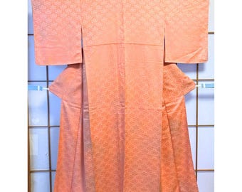 Könnte beinhalten: Ein pfirsichfarbener Kimono mit floralem Muster, ausgestellt auf einem Holzgestell. Das traditionelle japanische Kleidungsstück hat lange Ärmel und ein Wickeldesign. Der Stoff hat einen subtilen Glanz, und das florale Muster wiederholt sich über die gesamte Oberfläche.