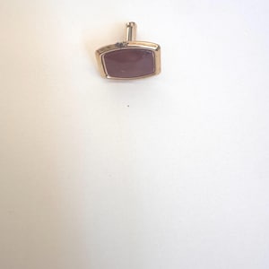 May include: A gold-toned rectangular cufflink with a maroon-colored stone center. The cufflink has a simple, classic design, suitable for formal wear. The cufflink is set against a plain white background.