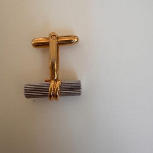 May include: Gold-toned cufflinks with a rectangular, silver-colored center section. The cufflinks have a classic design, with a gold bar connecting the two ends. The gold accents add a touch of elegance to the accessory.