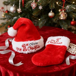 May include: A red Santa hat and stocking set with white trim. The hat and stocking are embroidered with "My 1st Christmas" and a name. A silver ribbon and pearl beads are on the red surface.