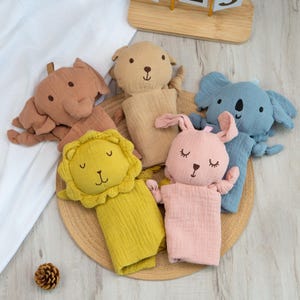 Pu&ograve; includere: Una collezione di morbidi burattini a forma di animali in vari colori. I burattini includono un elefante, un orso, un koala, un leone e un coniglio. Ogni burattino ha tratti del viso ricamati ed &egrave; realizzato in un tessuto strutturato. I burattini sono disposti su un tappetino intrecciato.