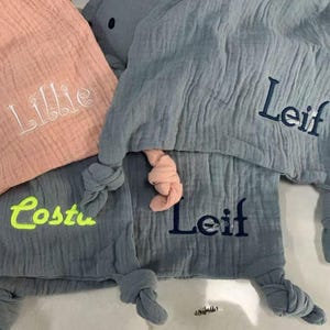 Pu&ograve; includere: Primo piano di tre coperte per bambini personalizzate. Una &egrave; color pesca con "Lillie" ricamato in bianco. Due sono blu-grigio, una con "Costa" in giallo neon e l'altra con "Leif" in blu navy.