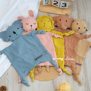 Pu&ograve; includere: Una collezione di morbide e soffici copertine di sicurezza per bambini in vari colori, ognuna con una testa di animale imbottita. Le coperte presentano teste di animali tra cui un koala, un coniglio, un leone, un elefante e un orso. Alcune coperte hanno nomi.