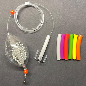 May include: A clear plastic fishing float containing silver ball bearings, attached to a coiled transparent fishing line with orange beads. A white plastic tube with three metal hooks and six colorful silicone tubes in white, pink, red, green, yellow, and orange.