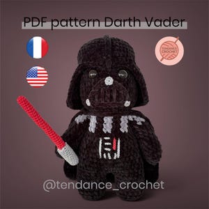 Könnte beinhalten: Gehäkelte Darth Vader-Puppe in Schwarz mit rotem Lichtschwert. Die Puppe hat einen detaillierten Helm und Brustplatten-Design. Das Bild enthält den Text "PDF pattern Darth Vader" und den Instagram-Handle "@tendance_crochet".