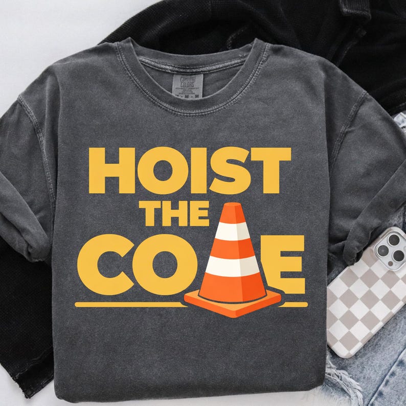 May include: Dark gray sweatshirt with the words "HOIST THE CONE" in yellow block letters. An orange and white traffic cone graphic is centered below the text. The sweatshirt is on a light-colored surface.