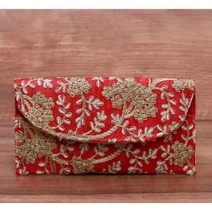 Op de afbeelding: Een rode clutch met gouden bloemenborduurwerk. De clutch heeft een klepsluiting en is versierd met ingewikkeld gouddraadwerk. Het ontwerp heeft een herhalend patroon van bloemen en bladeren, wat een elegante en sierlijke uitstraling creëert.