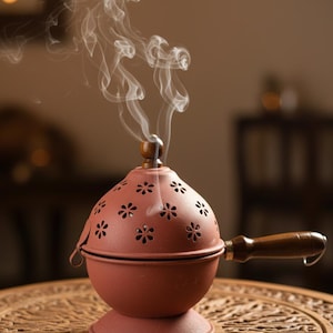 May include: A terracotta incense burner with a wooden handle and lid. The spherical burner features floral cutouts, with wisps of smoke rising. It sits on a carved wooden table. The measurements are in centimetres.