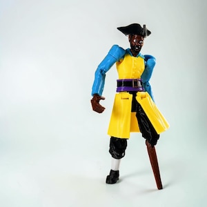 Peut inclure: Une figurine de pirate à la peau foncée, portant un tricorne noir, un gilet jaune, une ceinture violette et des manches bleues. La figurine présente un pantalon noir, des chaussettes blanches, des chaussures noires et une jambe de bois marron.