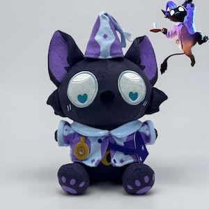 May include: A plush toy of a dark purple cat-like creature wearing a light blue and purple pointed hat and a matching jacket. The creature has large eyes with light blue heart-shaped pupils, a small black nose, and purple paw pads on its feet.