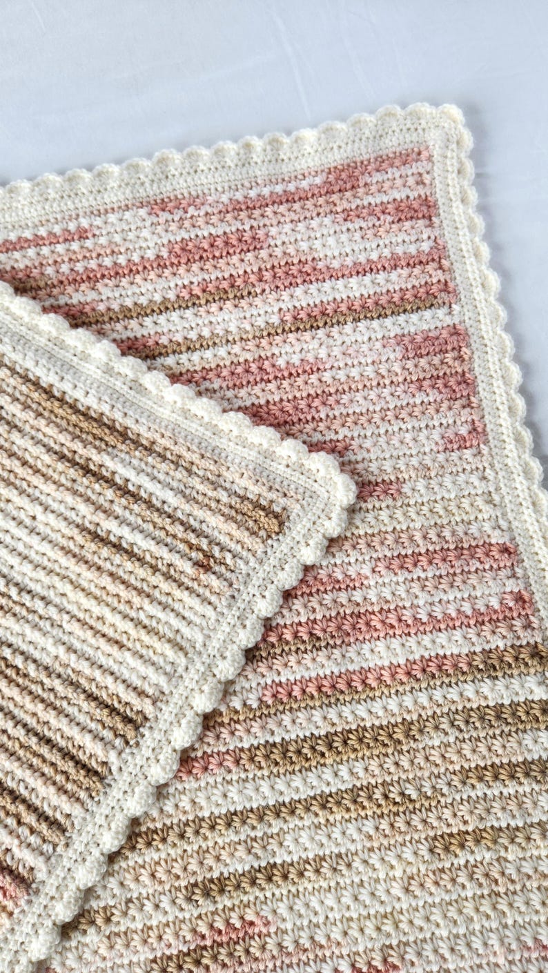 May include: A handmade crochet blanket in shades of pink, beige, and brown. The blanket has a striped pattern and a scalloped white border. The soft, textured blanket is suitable for a baby or as a decorative throw.