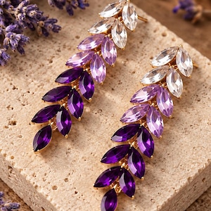Può includere: Un paio di lunghi orecchini pendenti con cristalli taglio marquise disposti a forma di foglia. I cristalli presentano una sfumatura di colore che va dal trasparente in alto al viola chiaro, viola medio e infine viola intenso alla base, montati su oro.