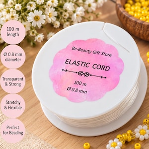 Könnte beinhalten: Eine weiße Kunststoffspule mit transparentem elastischem Band und einem rosa gewellten Etikett mit der Aufschrift Be-Beauty Gift Store, ELASTIC CORD, 100 m und 0,8 mm Durchmesser. Die Spule ist mit 100 Metern dehnbarem Band umwickelt.