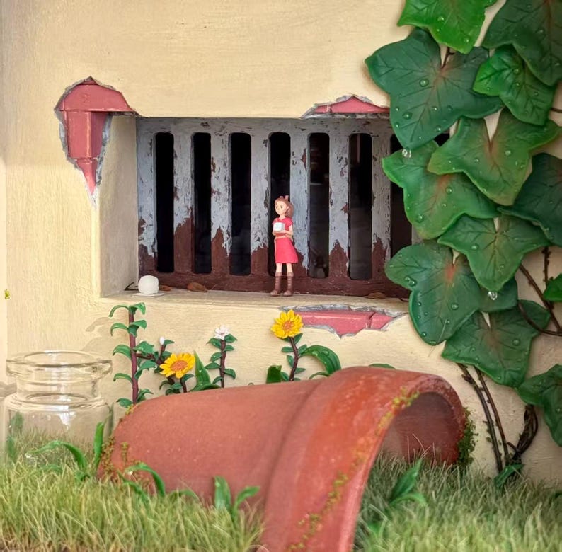 May include: A miniature diorama featuring a girl in a red dress standing near a sewer grate. A broken terracotta pot, grass, and flowers are in the foreground. Green leaves and a glass jar are also visible.
